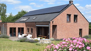 A brick house with a sloped roof, a patio with outdoor furniture, and a garden with pink flowers. - Villa in Belgium With Private Pool & Garden (Gesves)