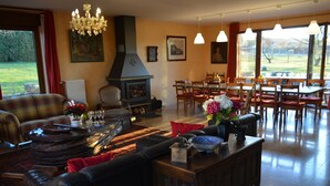 A spacious living room with a fireplace, a dining area with wooden furniture, and large windows offering a view of the outdoors. - Villa in Belgium With Private Pool & Garden (Gesves)
