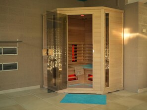 Una sauna con puerta de cristal, interior de madera y una toalla en el suelo.