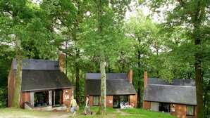 A rustic lodge with two brick buildings, each with a chimney, surrounded by lush greenery. - Nicely Furnished Bungalow with Fireplace near Maas (Hastiere)