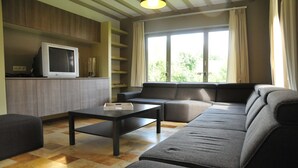 A modern living room with a sofa, a coffee table, a television, and a large window with curtains. - Holiday Home in Marche-en-famenne Near Train (Marche-en-Famenne)