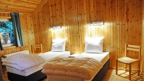 A wooden cabin room with two beds, a chair, and a window with curtains. - Holiday Home in Vielsalm With Lake View (Vielsalm)