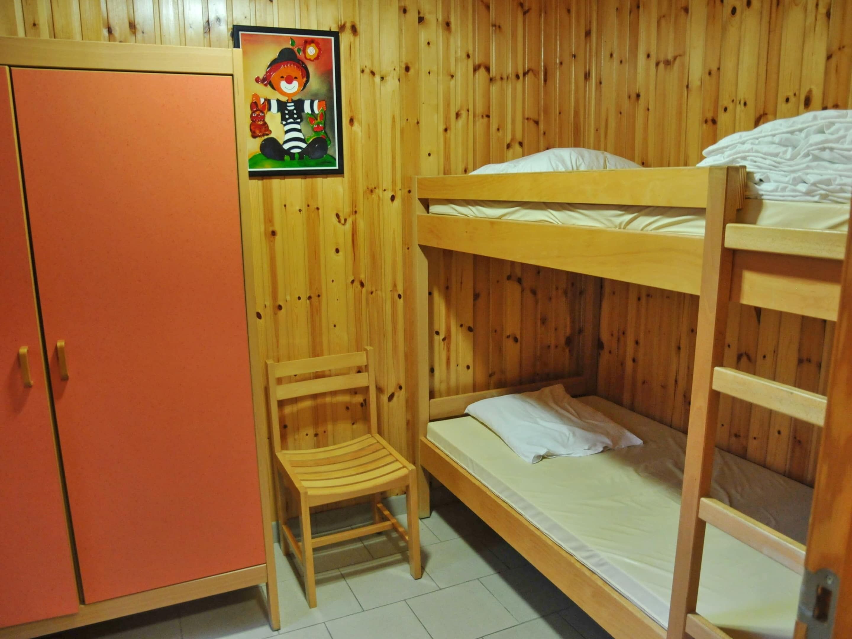 Een slaapkamer met een stapelbed, een houten garderobe en een kleine houten stoel.
