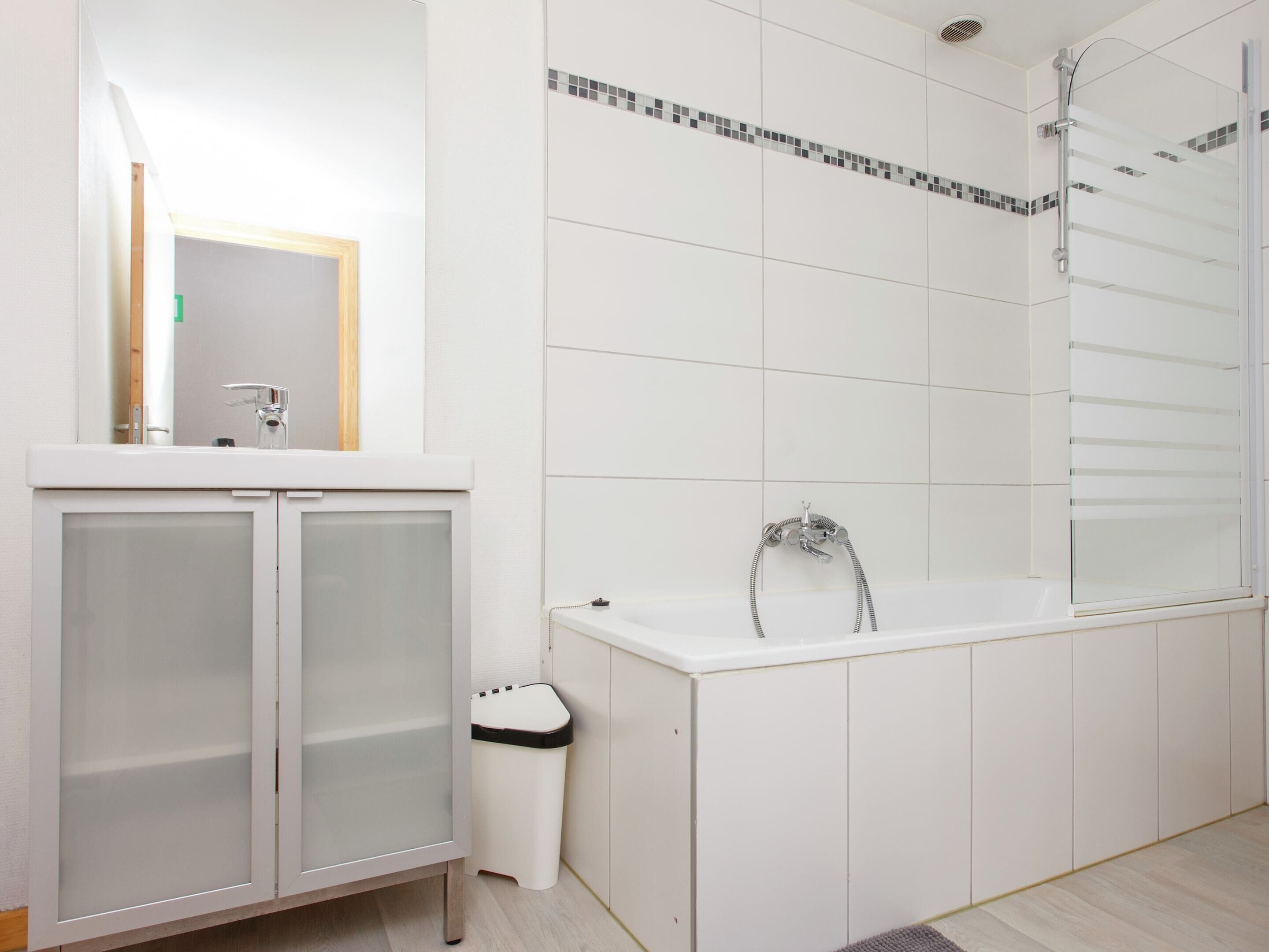 A modern bathroom with a white vanity, a glass-enclosed cabinet, a white toilet, and a bathtub with a showerhead.