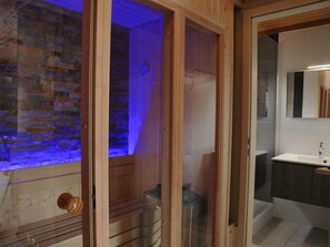 Une salle de bain avec une structure en bois, un mur en pierre, une cabine de douche en verre et un lavabo avec un miroir.