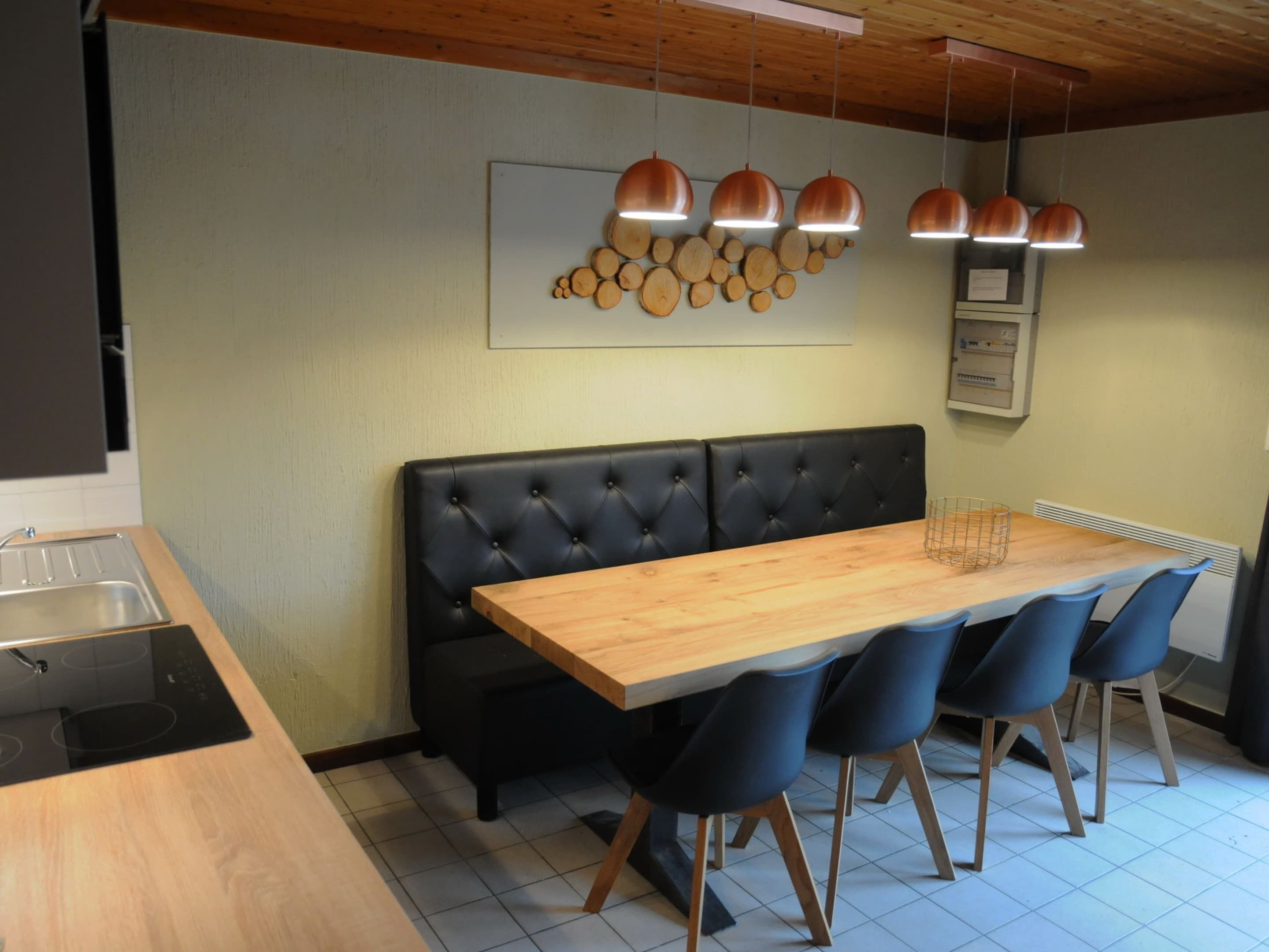 Une cuisine moderne avec un plan de travail en bois, un banc recouvert de tissu noir et des luminaires suspendus.