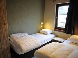 Ein Zimmer mit zwei Einzelbetten, einem kleinen Nachttisch, einem Fenster mit Vorhängen und einer Wandleuchte.