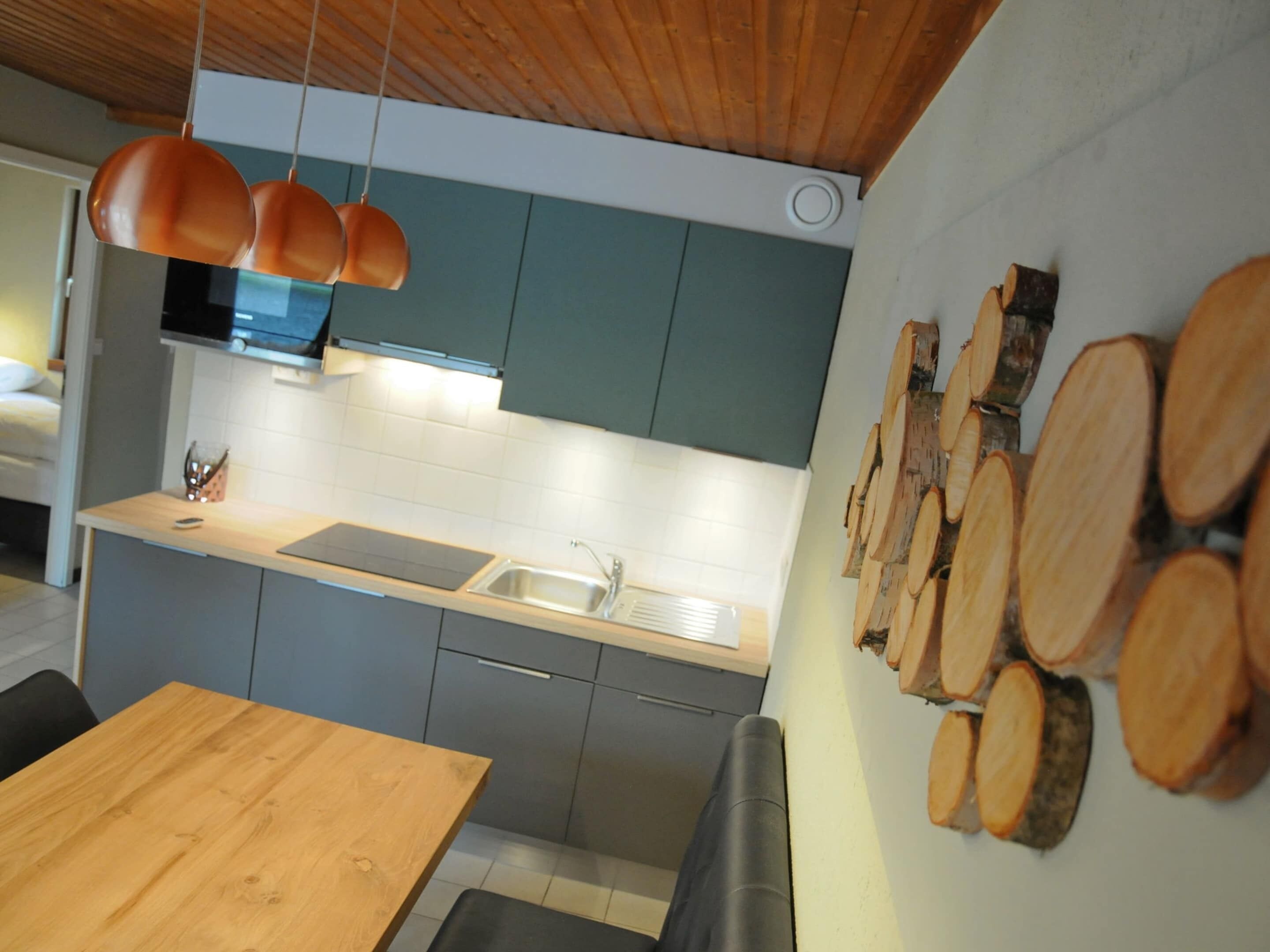 A modern kitchen with grey cabinets, a wooden dining table, and hanging pendant lights.