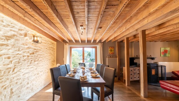 A dining area with a wooden table set for six, flanked by stone walls and wooden beams. - Lierneux Family Nature Stay (Lierneux)