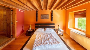 A bedroom with a wooden ceiling, a large bed with white bedding, two bedside tables with lamps, and a window with a view of greenery. - Lierneux Family Nature Stay (Lierneux)