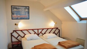 Una habitación pequeña y acogedora con dos camas individuales, cabecero de madera, un cuadro en la pared y un tragaluz.