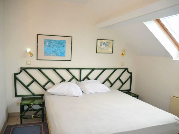 Une chambre à coucher avec un lit, deux tableaux encadrés, une table de chevet et une lucarne.