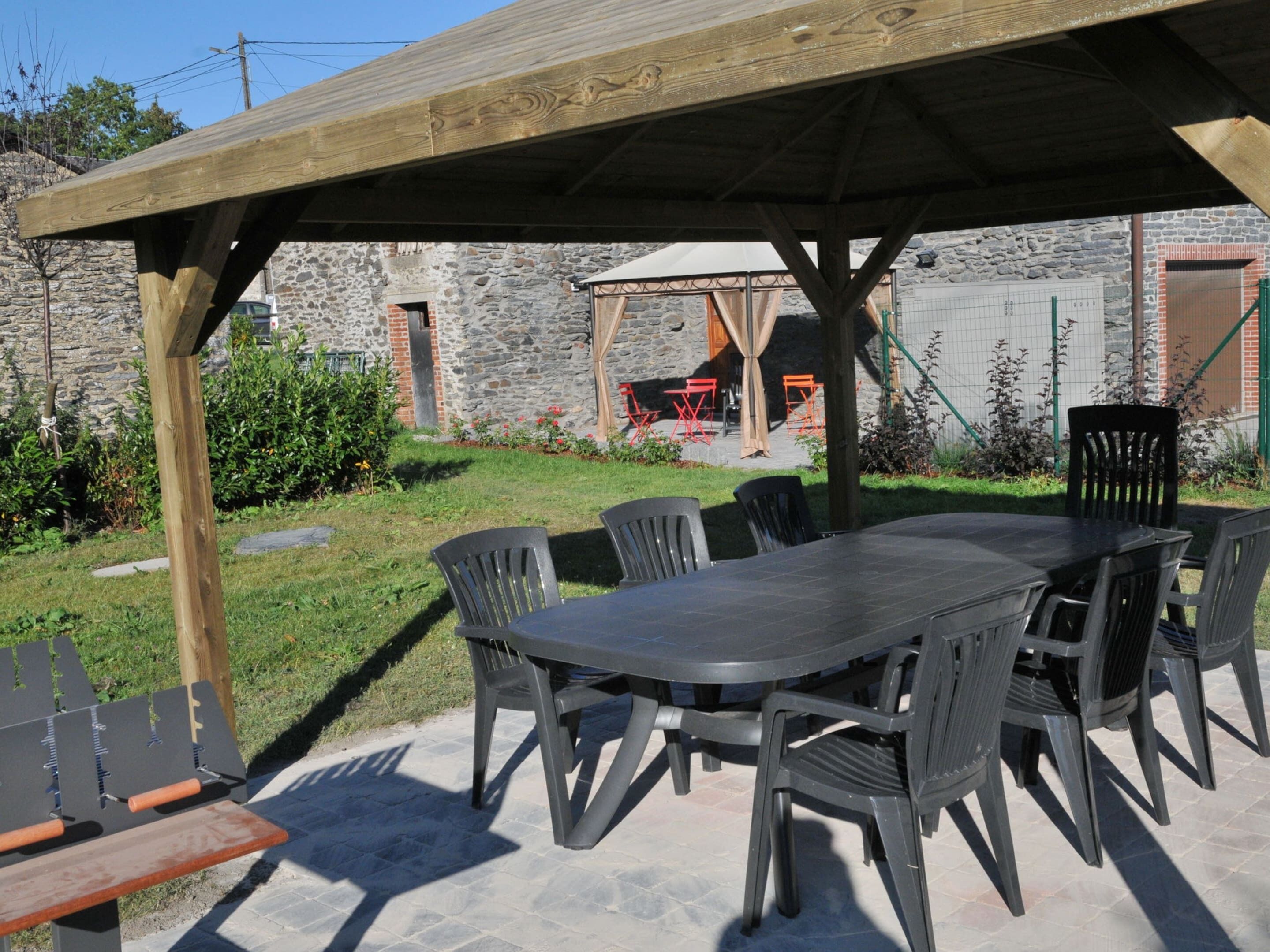 An outdoor patio with a wooden pergola, a stone wall, and a table with chairs.