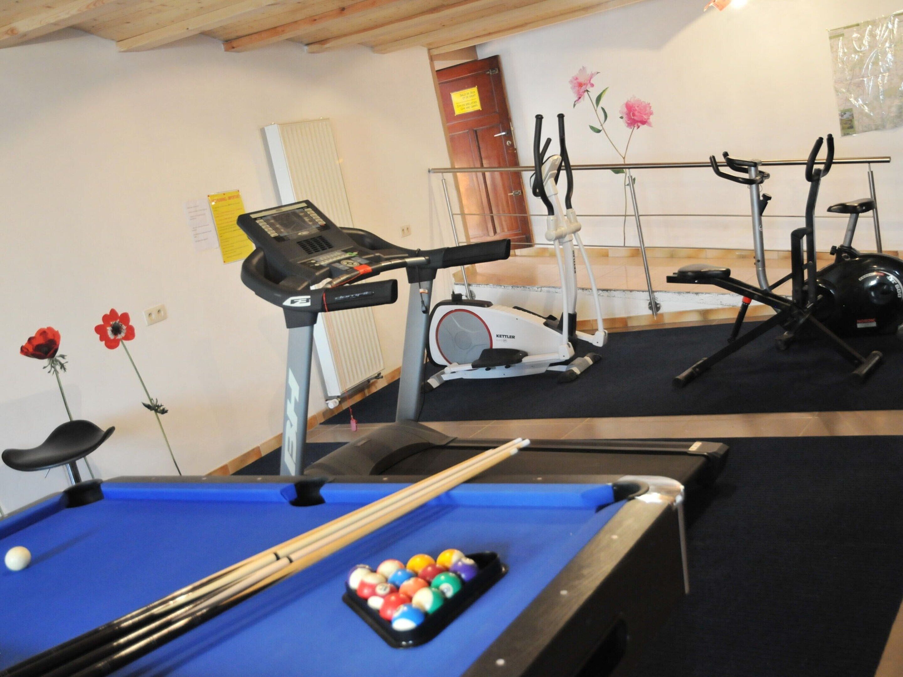 A room with a pool table, exercise equipment, and a door with a sign.