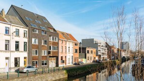 Un carrer al costat d'un canal amb edificis de diversos pisos, una ruta per a bicicletes i cotxes aparcats.