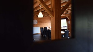 Un interior rústico con vigas de madera a la vista, un reloj y una zona de comedor con sillas y mesas.