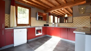 Una cocina con armarios rojos, lavavajillas, horno y una ventana con cortinas.