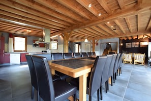 A spacious dining area with a long wooden table and black chairs, a kitchen with red cabinets, and a staircase leading to an upper level. - Rendeux Retreat With Sauna (Rendeux)