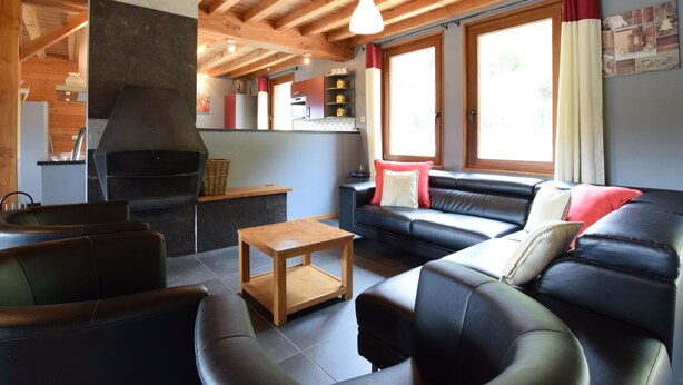 Una sala de estar acogedora con chimenea, sofás de cuero, una mesa de centro de madera y ventanas grandes con cortinas.