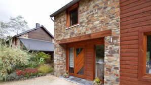 Una casa de piedra y madera con camino de grava y jardín con diversas plantas.