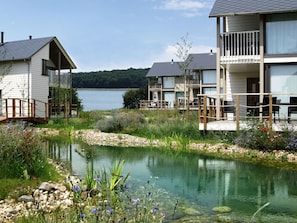 A lakeside property with a small pond, wooden deck, and a building with a balcony overlooking the water.