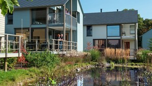 A modern two-story residential building with a balcony, a small pond, and surrounding vegetation. - Comfortable Villa With Stove, Located in a Lake Area (Froidchapelle)