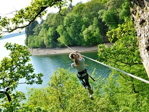 Una persona che vola su una zip-line sopra un lago, con una fitta foresta sullo sfondo.