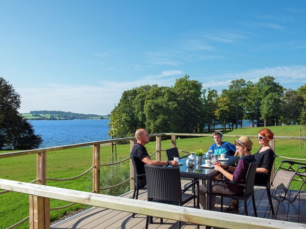 A group of people seated at a table on an outdoor deck with a lake view.