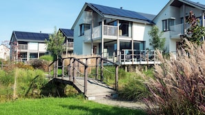 A modern residential building with solar panels, a covered balcony, and a wooden bridge. - Comfortable Villa With Stove, Located in a Lake Area (Froidchapelle)