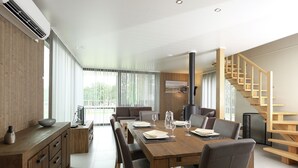 A modern dining area with a wooden table and chairs, a built-in stove, and a wooden staircase. - Comfortable Villa With Stove, Located in a Lake Area (Froidchapelle)
