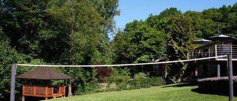 Un espace verdoyant bien entretenu, avec un filet de volley-ball, un banc en bois et un kiosque.