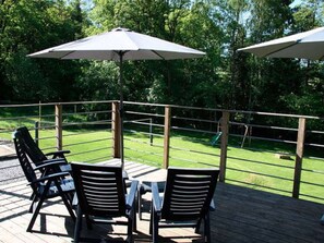 An outdoor deck with a table and chairs, surrounded by a wooden railing, overlooking a grassy area. - Luxurious Holiday Home With Sauna in Spa (Spa)
