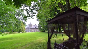 A gazebo with a canopy and a swing, surrounded by lush green grass and trees, with a large building in the background. - Delightful Castle in Bastogne with Hot Tub (Bastogne)