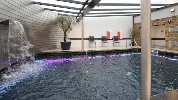 Piscina interior con cascada, zona de estar y planta en maceta.