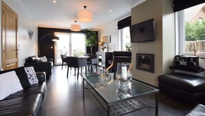 Una sala de estar moderna con una mesa de centro de vidrio, sofás de cuero, una zona de comedor con sillas, una chimenea y un televisor montado en la pared.