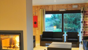 A cozy living room with a fireplace, comfortable seating, and a view of the outdoors. - Holiday Home in Houyet With Private Sauna (Houyet)