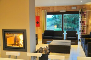 Ein gemütliches Wohnzimmer mit Kamin, bequemen Sitzmöglichkeiten und einem großen Fenster mit Blick ins Freie.
