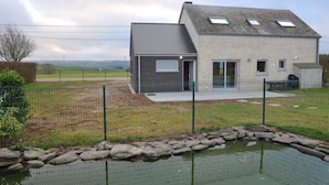 Une maison moderne à deux étages, dotée d’un toit en pente, d’une cour clôturée et d’un petit étang.