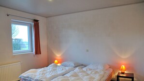 Une chambre à coucher avec un lit, deux lampes de chevet, une fenêtre avec des rideaux et un radiateur.