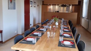A long dining table set for a meal with chairs around it, a vase with flowers, and a kitchen in the background. - Beautiful Holiday Home in Malmedy-beverce With Sauna (Malmedy)