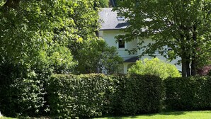 A well-maintained lawn with a hedge and trees in the foreground, and a two-story house with a visible window and door in the background. - Beautiful Holiday Home in Malmedy-beverce With Sauna (Malmedy)