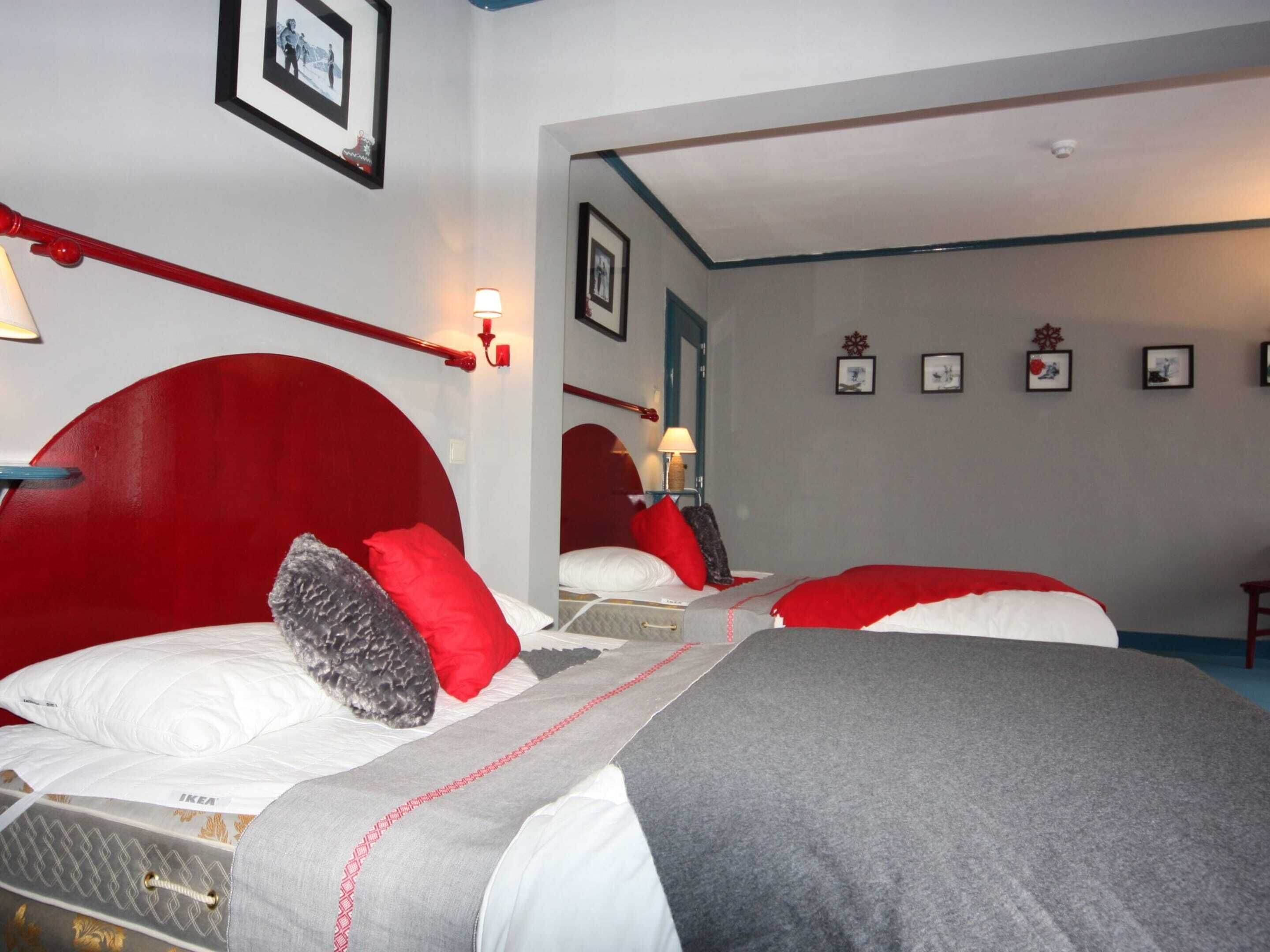 A hotel room with two beds, each with red headboards and white bedding. There are framed pictures on the walls and a mirror above the beds.
