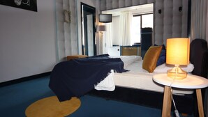 Ein Hotelzimmer mit einem Bett, einem Nachttisch mit Lampe, einem Fernseher und einem großen Fenster mit Vorhängen.