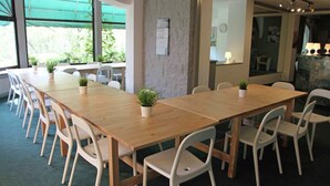 Ein Konferenzraum mit einem langen Holztisch, weißen Stühlen und Topfpflanzen.