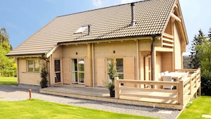 A wooden cabin with a sloped roof, large windows, and a wooden deck with outdoor seating. - Luxurious Villa with Sauna, Hot Tub, Recreation Room, Large Enclosed Garden (Durbuy)
