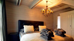 A bedroom with a large bed, a dark headboard, and a chandelier. - Luxurious Villa with Sauna, Hot Tub, Recreation Room, Large Enclosed Garden (Durbuy)