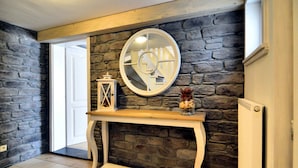 A room with a stone wall, a white console table, a mirror, and a door leading outside. - Luxurious Villa with Sauna, Hot Tub, Recreation Room, Large Enclosed Garden (Durbuy)