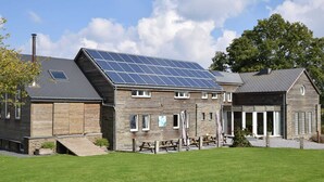A two-story building with a sloped roof, solar panels, and a wooden exterior. - Holiday Home in Ardennes With Pool & Sauna (Vielsalm)