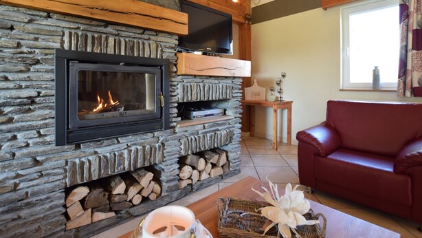 A stone fireplace with a TV above it, a red leather sofa, and a window with curtains. - Holiday Home in Ardennes With Pool & Sauna (Vielsalm)