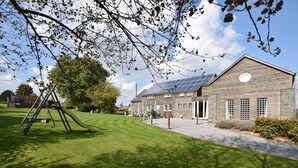 A building with a sloped roof, large windows, and a grassy lawn with a swing set. - Holiday Home in Ardennes With Pool & Sauna (Vielsalm)